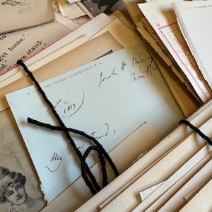 Bundle of over 100 vintage and antique paper ephemera pieces, including aged letters, postcards, and documents, arranged in a flat lay on a rustic wooden surface ready for scrapbooking and paper craft projects