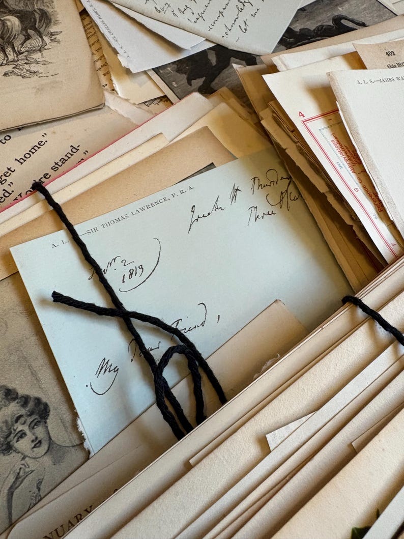 Bundle of over 100 vintage and antique paper ephemera pieces, including aged letters, postcards, and documents, arranged in a flat lay on a rustic wooden surface ready for scrapbooking and paper craft projects