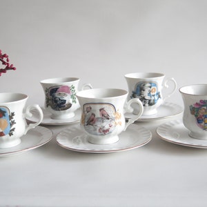 May include: Set of five white porcelain teacups and saucers. Each cup features a different colorful illustration, including a woman with apples, a gnome, birds on a branch, a portrait, and a group of children. The rims are trimmed with gold.