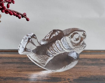May include: A clear glass sculpture of a fish with a detailed, textured surface. The fish is positioned with its head tilted upwards and its mouth slightly open.