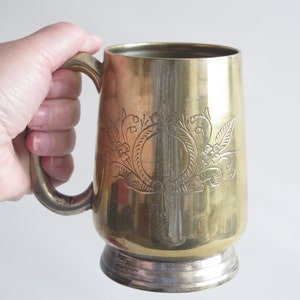 May include: A gold metal mug with a silver base and an engraved floral design.
