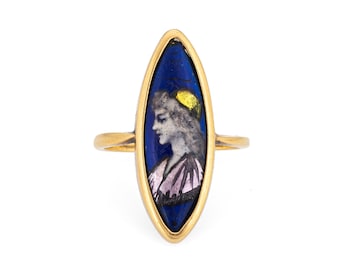 Puede incluir: Un anillo de oro con un camafeo de esmalte azul y blanco con el perfil de una mujer. El camafeo está engastado en un bisel en forma de marquesa.