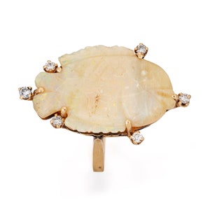 Puede incluir: Anillo de oro con una gran piedra de ópalo irregular en tonos blanco crema y amarillo. El ópalo está adornado con seis pequeños diamantes redondos engastados en garras de oro. El anillo tiene una banda de oro pulido simple.