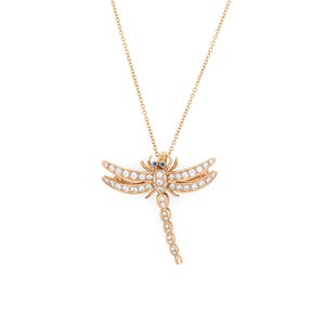 Può includere: Una collana con pendente a forma di libellula color oro. La libellula presenta un corpo e ali adornati con pietre preziose trasparenti. Gli occhi sono piccole pietre preziose blu. La catena della collana è anch'essa color oro.
