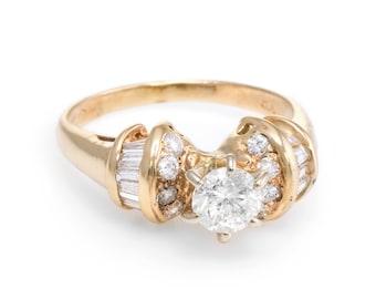 May include: A gold ring featuring a large, round, clear diamond center stone. The ring is accented with smaller, round diamonds and baguette-cut diamonds. The ring has a classic, elegant design.