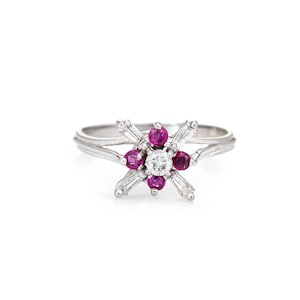 May include: A silver ring featuring a cluster of red rubies and a single diamond at the centre. The rubies are set in a flower design with diamond accents.