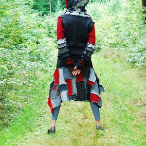 May include: A hooded jacket with a patchwork design in shades of gray, red, and black. The jacket has a long, flowing silhouette and a unique, layered design.