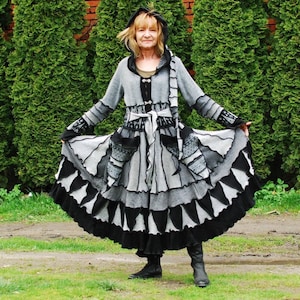 Könnte beinhalten: Ein langärmliges Kleid in Grau und Schwarz mit einem Rüschenrock und einer Kapuze. Das Kleid ist aus weichem, gestricktem Stoff und hat einen Gürtel.