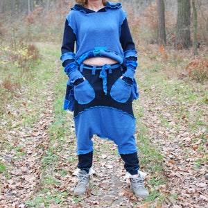 May include: A woman wearing a blue and black hooded top with a blue and black pair of trousers. She is standing in a woodland setting.