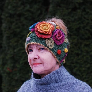 Puede incluir: Una mujer con una diadema de ganchillo verde con flores de colores y un suéter gris.