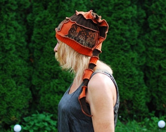 May include: A woman wearing a brown and orange knitted hat with a long tail. The hat has a unique design with a mix of textures and colors.