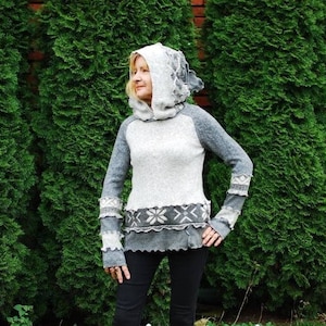 Könnte beinhalten: Ein grauer und weißer Pullover mit Kapuze und einem Schneeflockenmuster. Der Pullover hat einen geschichteten Look mit einem grauen und weißen Besatz am Saum und an den Ärmeln.