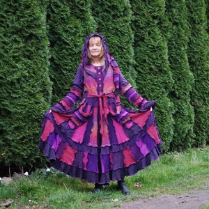 May include: A long, purple and pink hooded coat with a ruffled hem. The coat is made of patchwork fabric and has a belt.