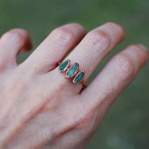 Puede incluir: Un anillo con tres piedras de color verde esmeralda engastadas en una banda de oro rosa.