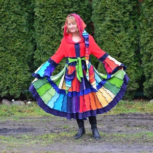 May include: A colourful, multi-layered dress with a red hooded top and a green sash. The dress features a rainbow of colours, including blue, green, yellow, orange, and purple.