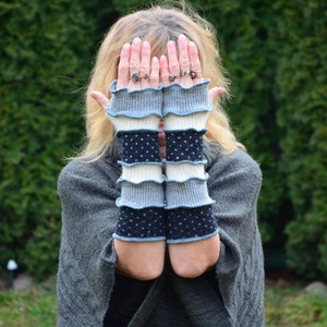 Könnte beinhalten: Ein Paar fingerlose Handschuhe in blau, weiß und schwarz mit einem gekräuselten Rand. Die Handschuhe sind aus weichem, gestricktem Stoff.