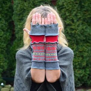 May include: A pair of gray fingerless gloves with red and yellow knit patterns. The gloves are folded over at the wrist and have a ruffled edge.