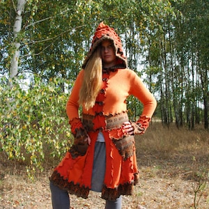 Könnte beinhalten: Ein langer, orangefarbener Kapuzenmantel mit braunen Akzenten und einem Patchwork-Design. Der Mantel hat einen Knopfverschluss und Taschen. Das Model trägt den Mantel mit grauen Leggings und roten Stiefeln.