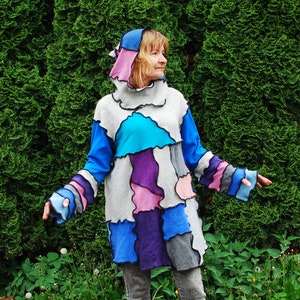 Puede incluir: Un suéter con capucha de patchwork colorido con una mezcla de telas azul, morado, rosa y gris. El suéter tiene un corte holgado y una silueta larga y fluida.