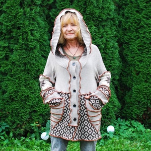 May include: A woman wearing a beige hooded cardigan with brown trim and a geometric pattern. The cardigan has a button closure and pockets.