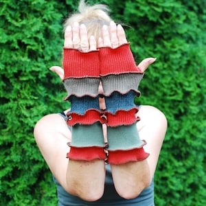 Puede incluir: Un par de guantes sin dedos de color rojo, verde y azul con un borde rizado. Los guantes están hechos de un tejido suave y de punto.