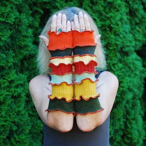以下が含まれることがあります： フリルのあるカラフルなニットの腕カバーのペア。腕カバーは柔らかく暖かい素材で作られており、赤、オレンジ、黄色、緑、青など、さまざまな色があります。