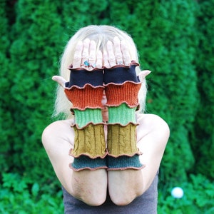 Könnte beinhalten: Ein Paar bunte Fingerlose Handschuhe mit einem Rüschenrand. Die Handschuhe sind aus weichem, gestricktem Stoff und in verschiedenen Farben gehalten, darunter Schwarz, Orange, Grün und Braun.