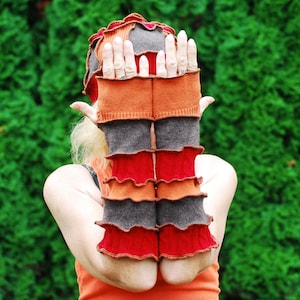 Puede incluir: Un par de guantes sin dedos multicolores con un diseño de volantes. Los guantes están hechos de una tela suave de punto y presentan una combinación de colores naranja, rojo, marrón y gris.