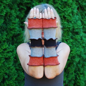 May include: A pair of long, knitted arm warmers with a layered design. The arm warmers are made of a soft, textured fabric in shades of gray, black, and orange.
