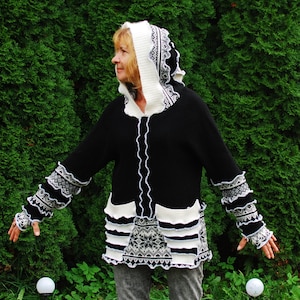 Puede incluir: Un suéter con capucha de punto negro y blanco con ribete blanco y un patrón geométrico. El suéter tiene una cremallera y bolsillos.