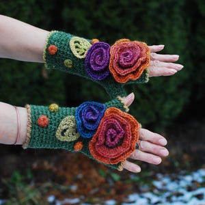 May include: A pair of green fingerless gloves with crocheted flower embellishments in shades of purple, orange, and red.