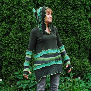 Puede incluir: Una mujer lleva una túnica con capucha verde y negra con un diseño de capas y volantes. La túnica tiene manga larga y está hecha de una tela suave y cómoda.