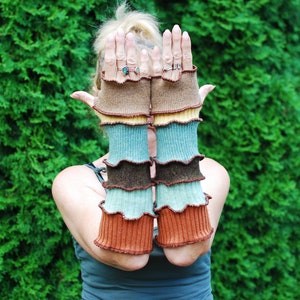 Könnte beinhalten: Ein Paar fingerlose Handschuhe in Braun, Blau und Grün mit einem gekräuselten Rand. Die Handschuhe sind aus weichem, gestricktem Stoff.