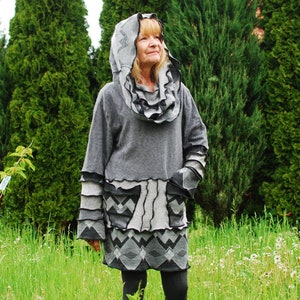May include: A grey hooded sweater with a ruffled neckline and a geometric pattern. The sweater has a long, loose fit and is made of a soft, comfortable fabric.