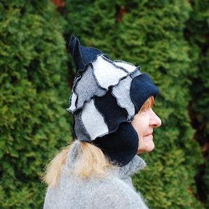 May include: A woman wearing a black and white patterned hat with ear flaps. The hat is made of felt and has a unique, whimsical design.
