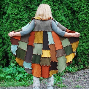 May include: A patchwork vest made from different coloured fabrics, with a brown, green, and orange colour scheme. The vest is worn by a person standing in front of a green hedge.