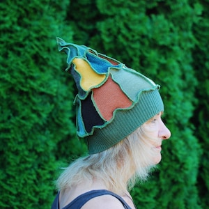 May include: A woman wearing a green, blue, yellow, brown and black patchwork hat with a pointed top.
