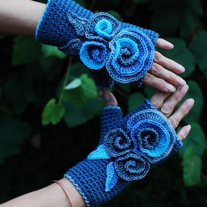 May include: A pair of blue crochet fingerless gloves. Each glove features a floral design with layered, swirling petals in shades of blue. The gloves are a dark blue with lighter blue accents.