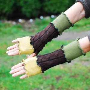 Könnte beinhalten: Ein Paar fingerlose Handschuhe in einem braunen, grünen und gelben Farbschema. Die Handschuhe sind aus einem weichen, gestrickten Stoff gefertigt und haben ein einzigartiges, mehrschichtiges Design.