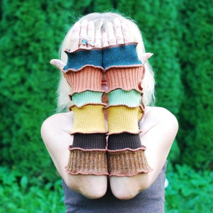 May include: A pair of colorful fingerless gloves with a ruffled edge. The gloves are made of a soft, knitted fabric and feature a variety of colors, including brown, green, yellow, and blue.