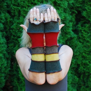 Puede incluir: Un par de guantes sin dedos a rayas con un esquema de color verde oscuro, rojo, marrón y amarillo. Los guantes están hechos de un tejido suave y de punto.