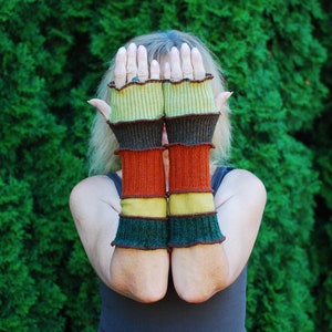 May include: A pair of colorful fingerless gloves with a green, brown, orange, and yellow striped pattern. The gloves are made of a soft, knitted fabric.