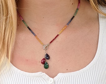 May include: A rainbow gemstone necklace with a silver clasp and a pendant featuring three teardrop-shaped gemstones in red, green, and blue.