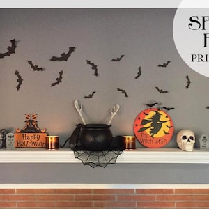 Op de afbeelding: Een Halloween-display met een wit schap met diverse decoraties. Inclusief een ketel, schedel, vleermuizen en een bord met "Happy Halloween". De tekst "Spooky Bat Printable!" is ook zichtbaar.