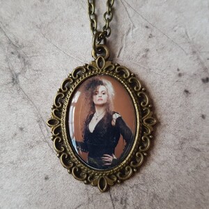 May include: A bronze oval pendant necklace with a cameo featuring a portrait of a woman with dark hair and a black dress. The cameo is set in a decorative frame.