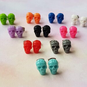 May include: A set of 10 pairs of skull stud earrings in various colors, including black, white, red, orange, green, blue, purple, pink, gray, and turquoise.