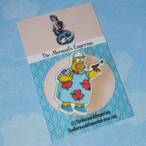 May include: A yellow cartoon character wearing a blue and pink Hawaiian shirt and a white cap, holding a red and brown object. The character is on a white background with blue and white patterned border. The text "The Mermaid's Emporium" is on the card.