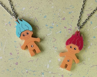 May include: Two troll doll necklaces with silver chains. One troll has blue hair and the other has red hair. Both trolls have orange skin and a silver belly button.