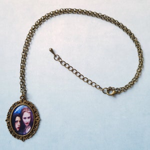 May include: An antique brass-toned necklace featuring a pendant with a portrait of two women. The oval pendant has a decorative frame. The chain has an adjustable length with a lobster clasp.