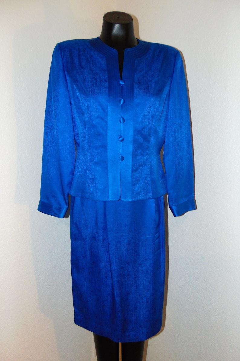 May include: A royal blue skirt suit with a button-up jacket and a matching skirt. The fabric has a subtle textured pattern.